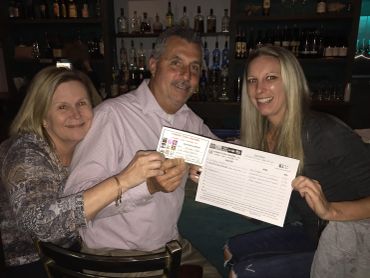Three people smiling and holding a menu and receipt at a bar.
