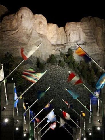 Mount Rushmore at night with flags.