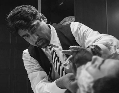 Barber carefully shaving a customer's face in a dimly lit room.