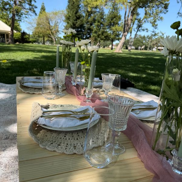 Elegant outdoor table setting with flowers, candles, and glassware on a wooden picnic table.