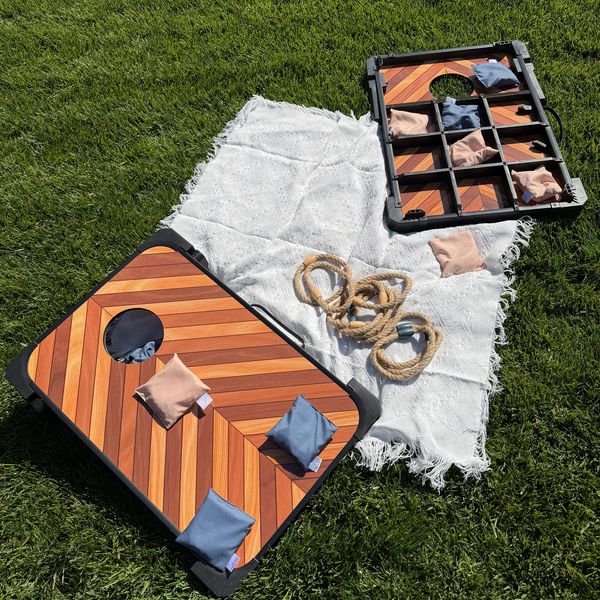 Outdoor bean bag toss game set up on grass with a white blanket and rope.