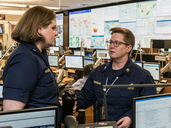 Two uniformed professionals discussing work in a busy control room.