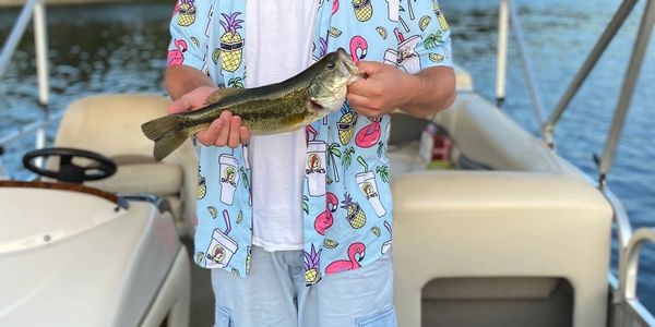 Person holding a largemouth bass on a boat with a colorful shirt.