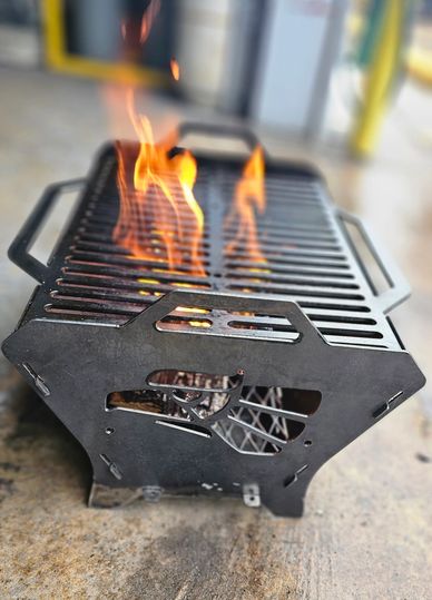 Metal portable grill with flames rising from it on concrete surface.