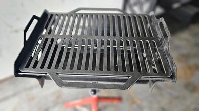 Close-up of a metal grill grate with handles on a stand.