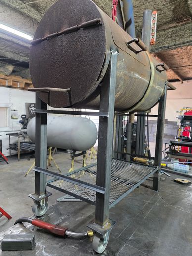 A large metal barrel smoker on a wheeled stand in a workshop.
