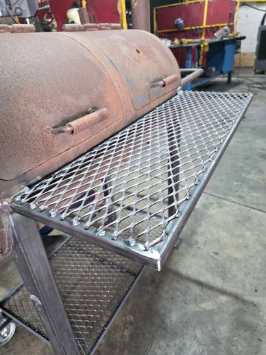 Close-up of a metal grill attached to a rusted barbecue smoker.