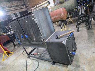 Metal smoker grill with wood stove in a workshop.