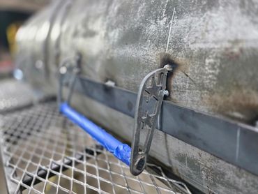 Close-up of a metal latch on a weathered cylindrical tank.