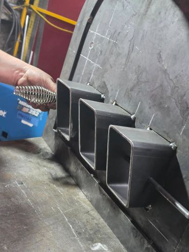 Hand holding a spring handle near three metal rectangular tubes welded on a surface.