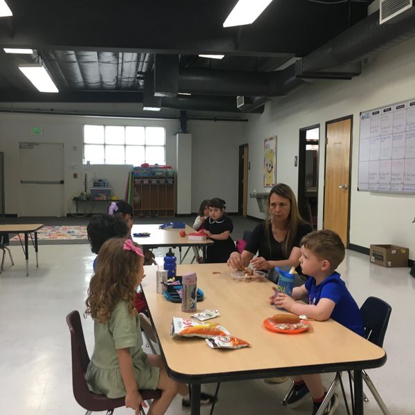 Teacher and children sitting around a table during snack time in a classroom.