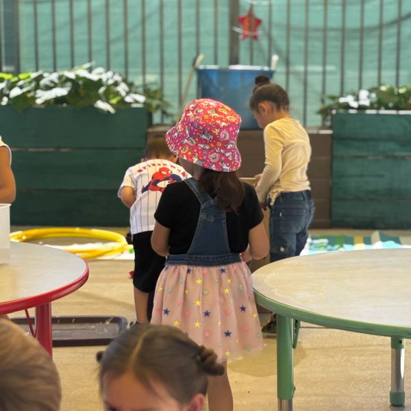 Children playing indoors, one girl wearing a colorful hat and dress.