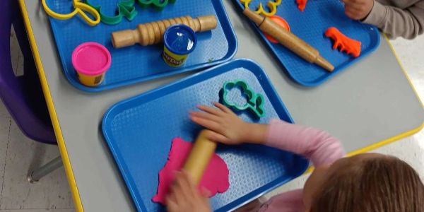 Children playing with colorful playdough and rolling pins.