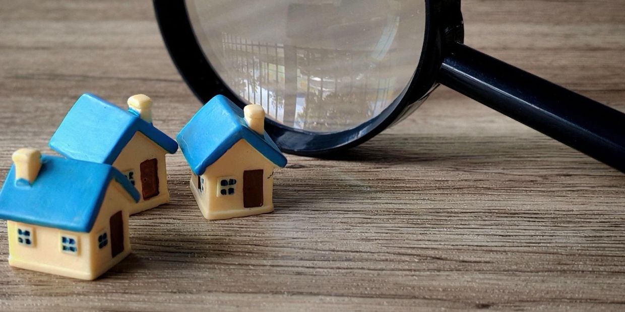 Three small model houses with blue roofs beside a magnifying glass on a wooden surface.