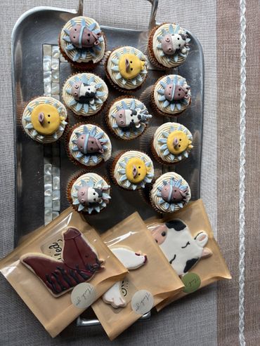 Cupcakes decorated with farm animals and cookies on a tray.