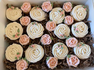 Cupcakes decorated with white and pink rose frosting in a box.