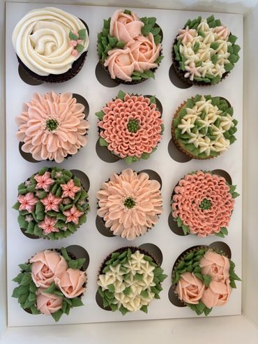 A box of twelve beautifully decorated floral cupcakes with pastel pink and green icing.
