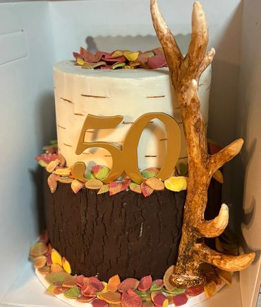Two-tiered rustic cake with autumn leaves and antler decoration for a 50th celebration.