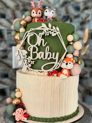 Two-tier baby shower cake with woodland animal decorations and 'Oh Baby' topper.