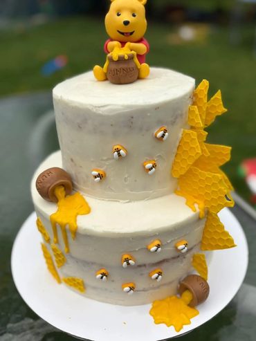 Two-tier Winnie the Pooh cake with honey and bees decorations.