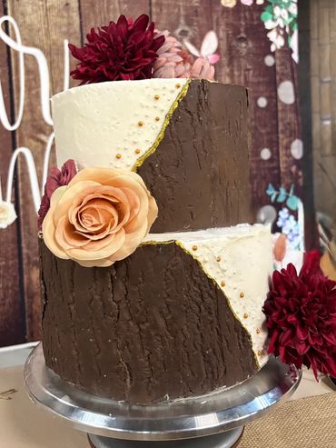 Two-tiered cake with chocolate and white frosting, decorated with gold accents and flowers.