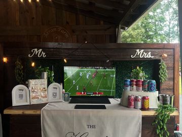 Wedding bar setup with Mr. and Mrs. signs and a TV showing football.