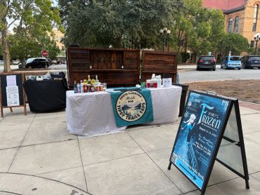 Outdoor market stand with beverages and a Frozen 2 event sign.