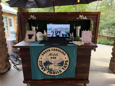Portable bar setup under an umbrella with Mr. and Mrs. signs.