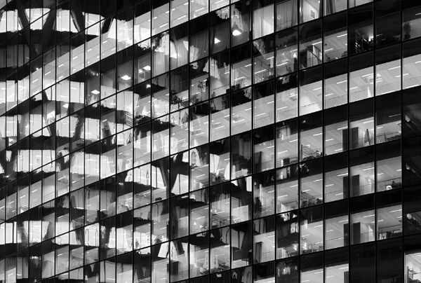 Black and white photo of an office building's glass façade with interior reflections.