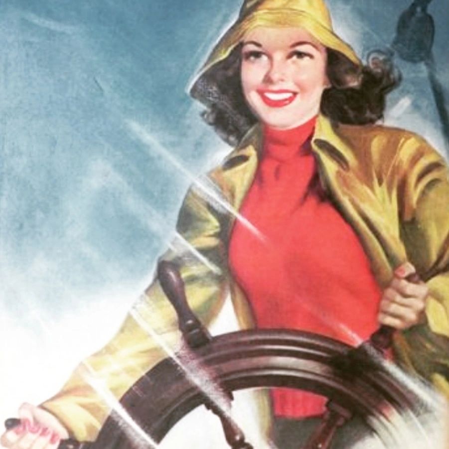 Smiling woman in yellow raincoat steering a ship's wheel.