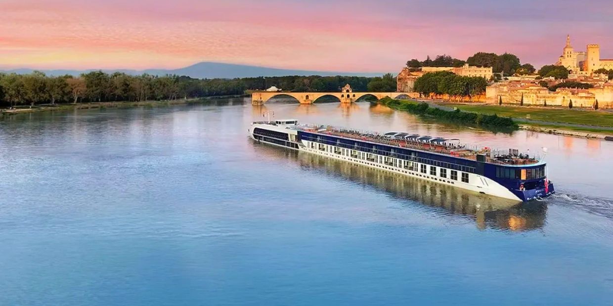 River cruise ship sailing near a historic bridge at sunset.