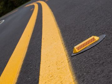 Close-up of yellow road lines and reflective marker on asphalt.