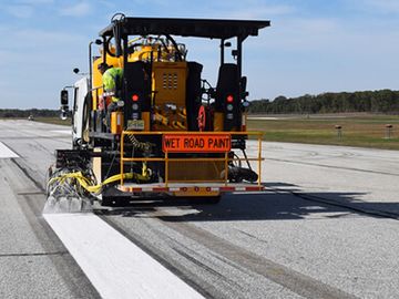 Machine painting fresh white lines on a road under clear sky.