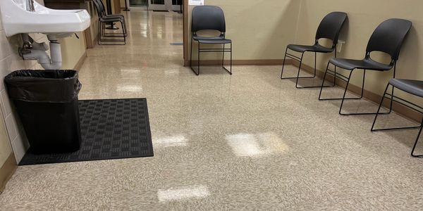 Empty waiting area with chairs, sink, and trash can in a hallway.