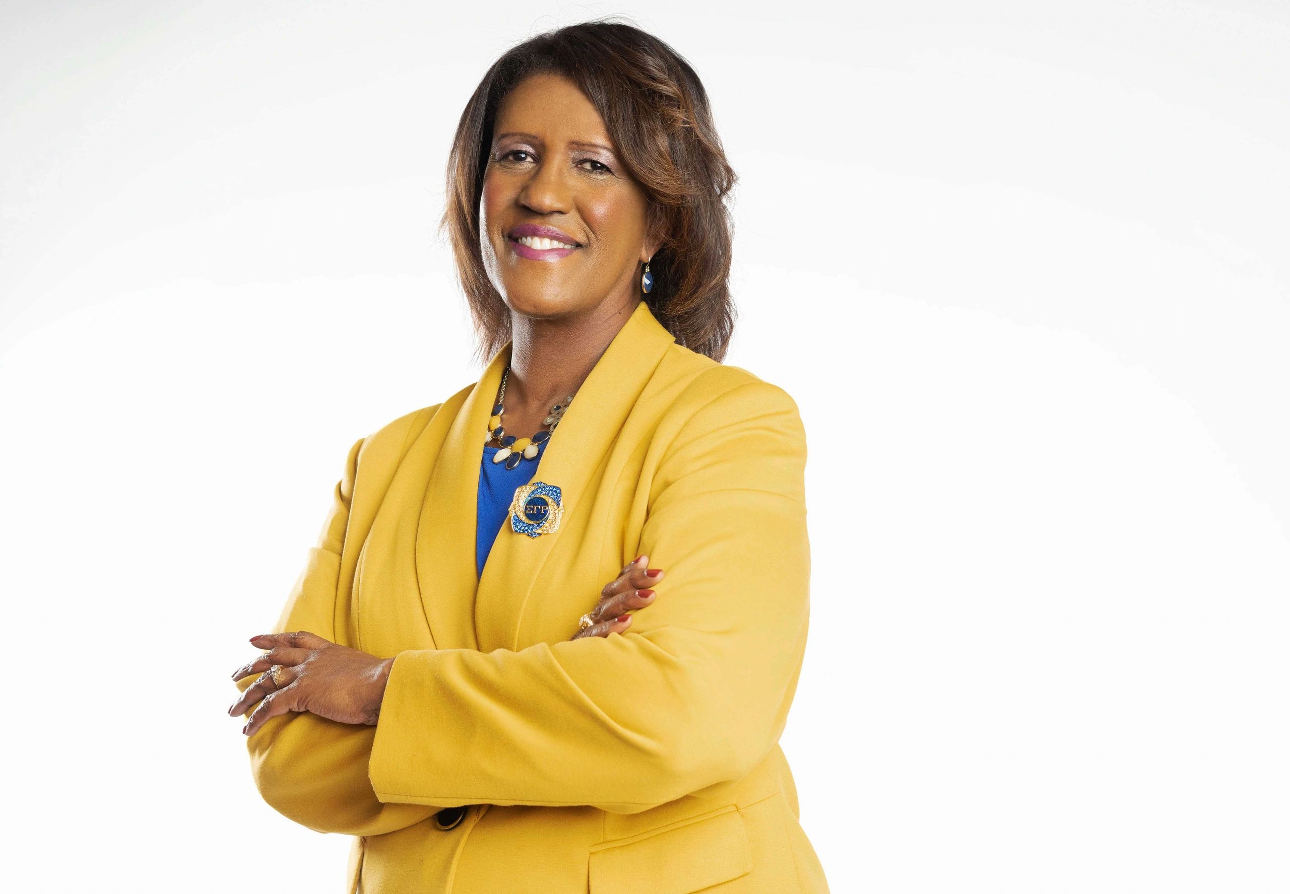 Confident woman in a yellow blazer smiling with arms crossed.