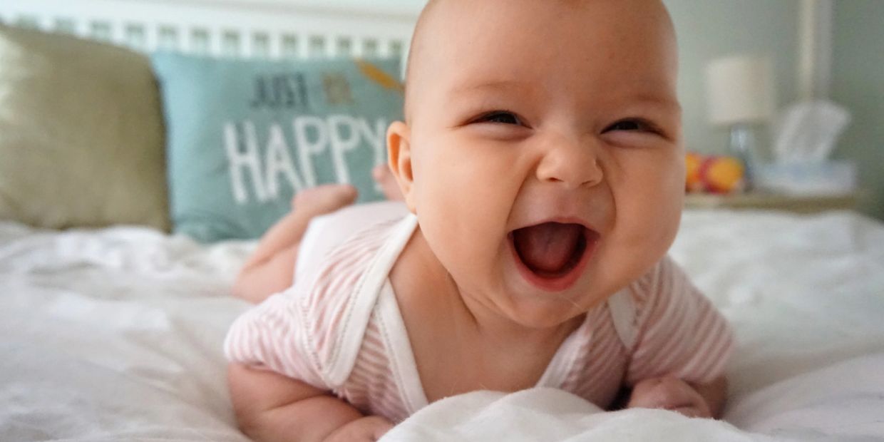 A joyful baby laughing happily on a bed.