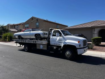Tow truck carrying a luxury SUV in a suburban neighborhood.
