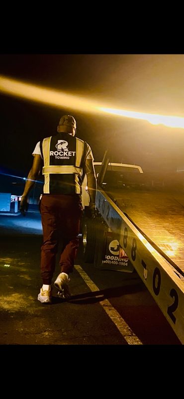 Towing worker walking beside a tow truck at night.
