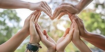 Multiple hands forming a heart shape together outdoors.