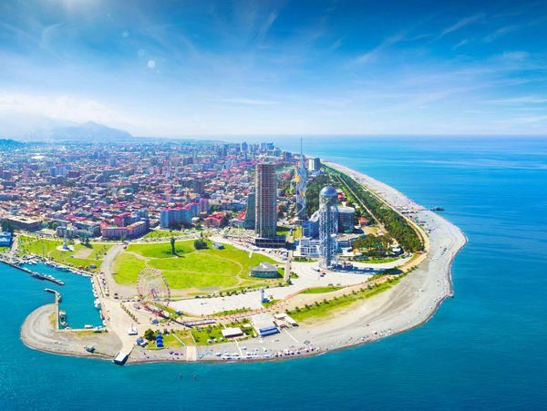 A coastal city with modern buildings and a ferris wheel by the beach.