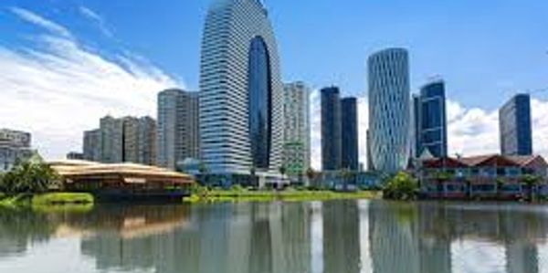 Modern skyscrapers reflected on a calm river under a blue sky.