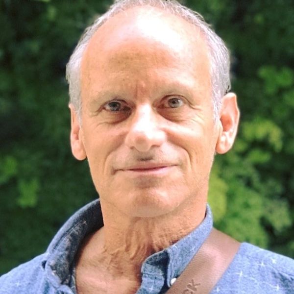 Portrait of a middle-aged man smiling outdoors with greenery in the background.