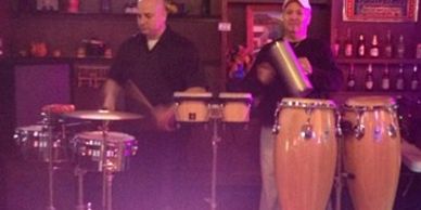 Two men playing various percussion instruments in a cozy setting.