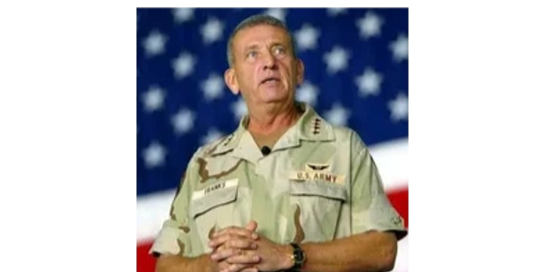 General Tommy Franks stands before an American flag.