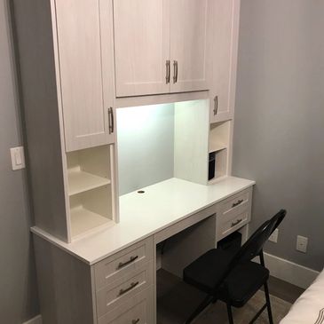 White desk with storage cabinets and a black folding chair in a bedroom corner.