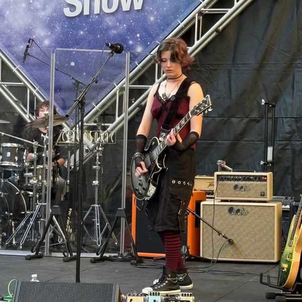 Young musician playing electric guitar on stage during a live performance.