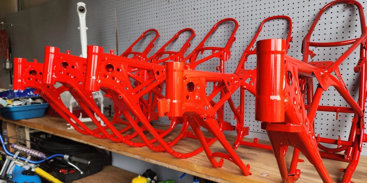 Bright red motorcycle frames lined up on a workbench in a workshop.