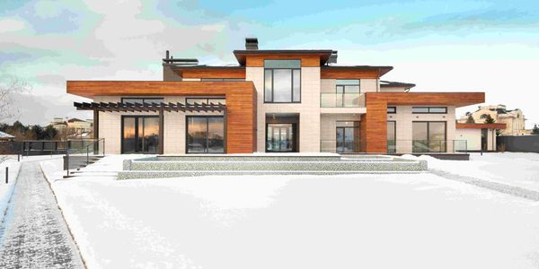 Modern two-story house with wood and stone exterior in snowy landscape.