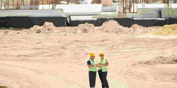 Two construction workers discussing plans at a dusty construction site.