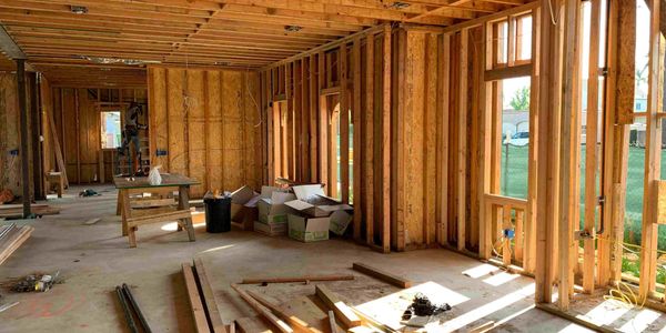Interior of a wooden house under construction with exposed beams and sunlight.
